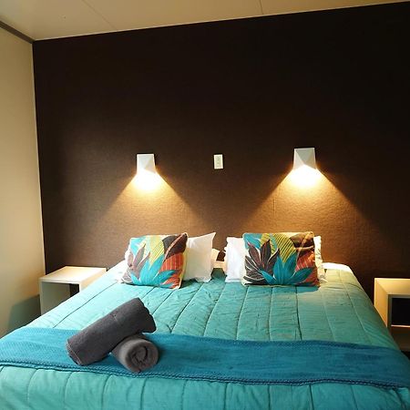 Taupo Debretts Spa Resort Luaran gambar The image shows a bedroom with a modern and inviting layout. The focal point is a bed with a vibrant turquoise comforter, decorated with two colorful pillows featuring floral patterns. On either side of the bed, there are small nightstands with wall-