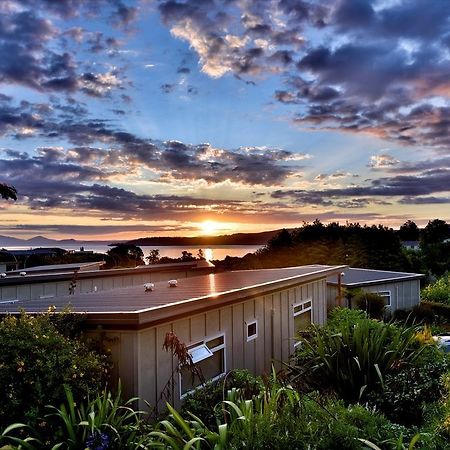 Taupo Debretts Spa Resort Luaran gambar The photo depicts a serene landscape during sunset. In the foreground, there is a modest building partially covered by greenery. The roof of the building is visible, along with some windows. Surrounding the structure are lush plants and foliage. 

In