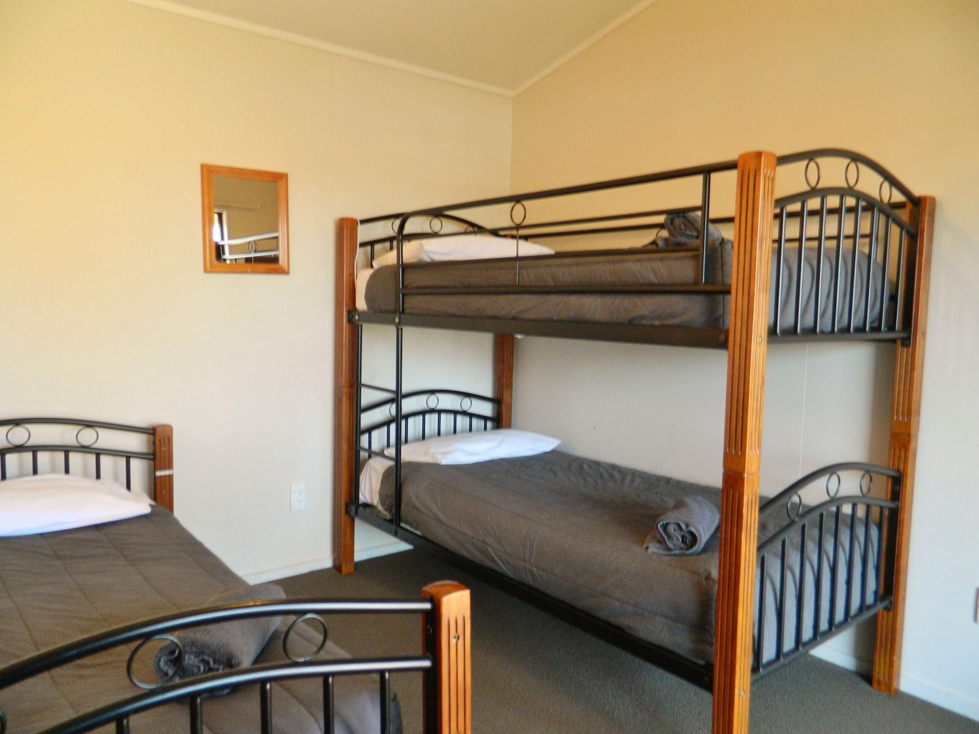 Taupo Debretts Spa Resort Luaran gambar The photo shows a room with two types of beds. There is a sturdy wooden bunk bed with two levels of sleeping space, each having a grey mattress and a pillow. Next to it, there is a single bed with a similar grey mattress and a pillow. The room has pl
