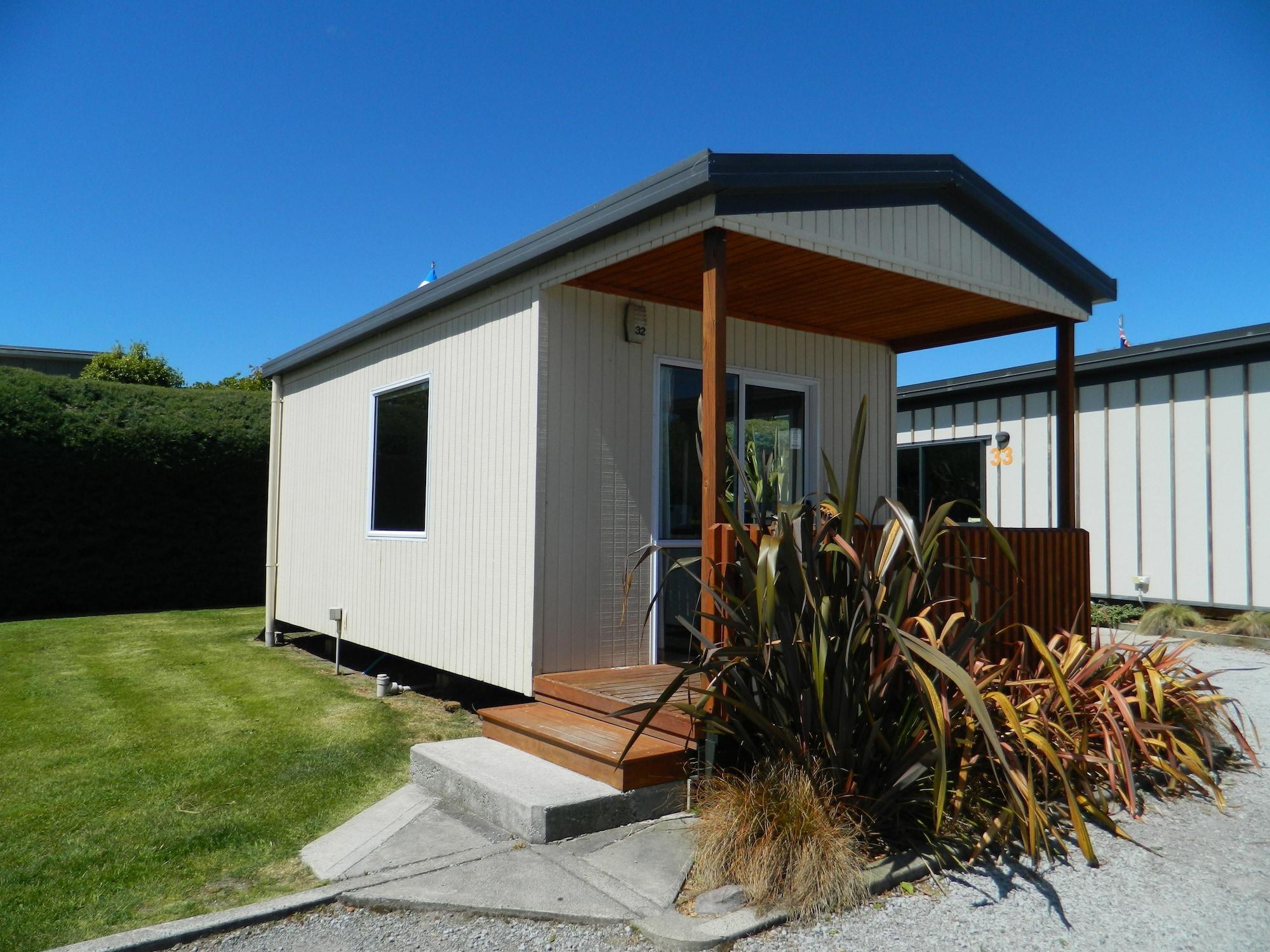 Taupo Debretts Spa Resort Luaran gambar The photo shows a small, modern cabin or vacation home. It features a light-colored exterior with a a small porch at the entrance. The porch has wooden steps that lead up to the front door. Surrounding the cabin is a neat lawn, with some landscaping 