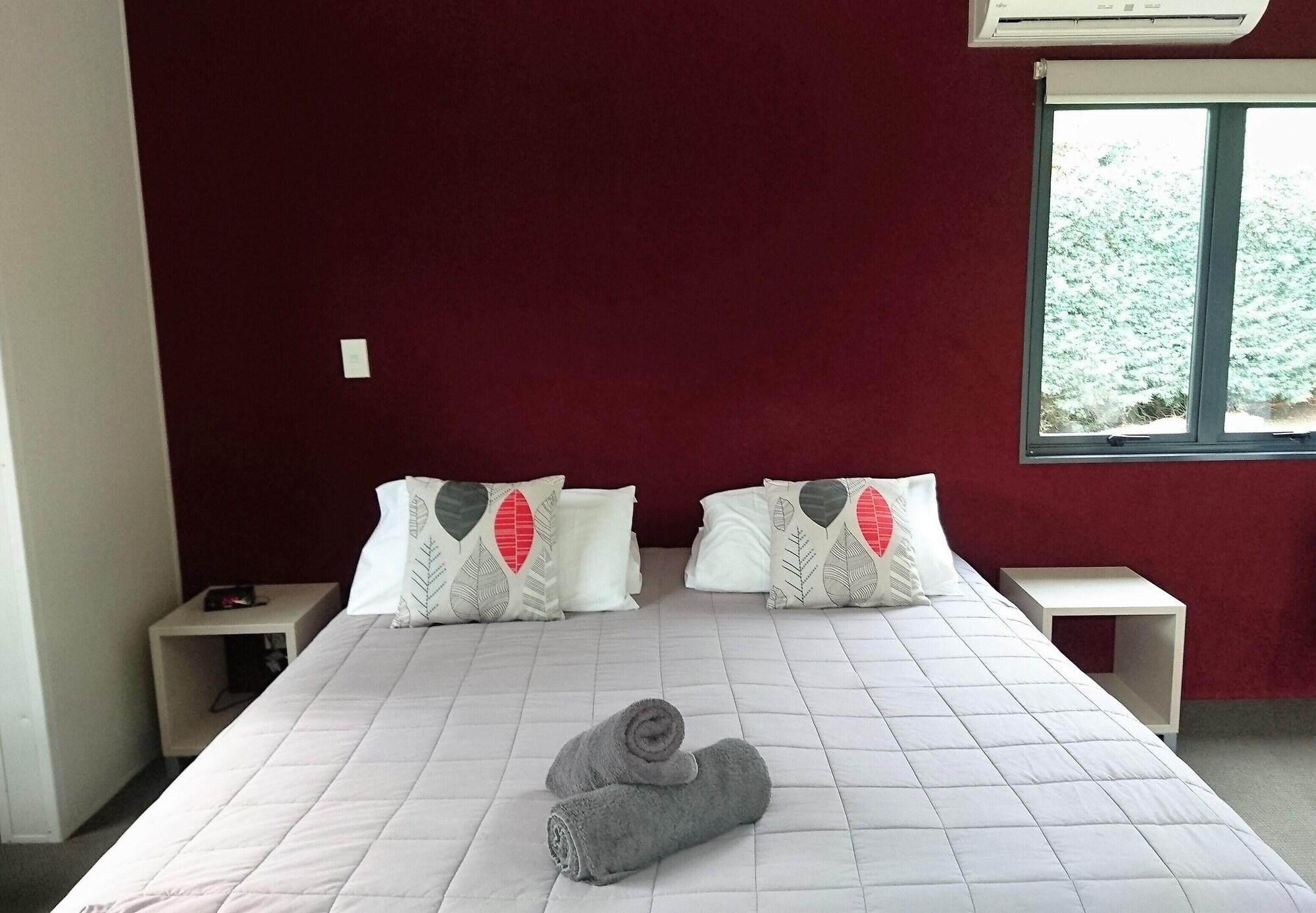 Taupo Debretts Spa Resort Luaran gambar The photo shows a cozy bedroom featuring a large bed with a light-colored quilt. The bed has two decorative pillows with a simple design on each side. There are two bedside tables, one on each side of the bed. On the bed, there are rolled towels plac