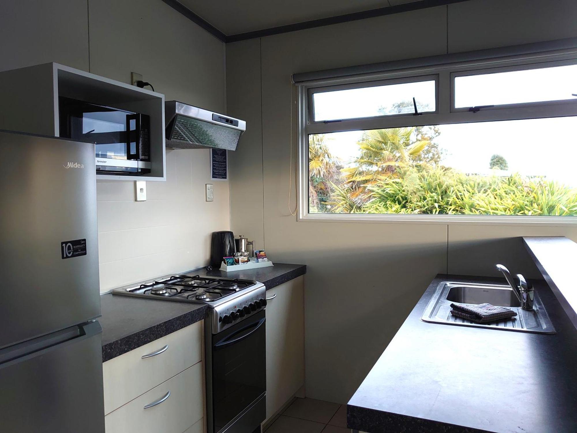 Taupo Debretts Spa Resort Luaran gambar The photo shows a kitchen equipped with modern appliances. On the left side, there is a refrigerator and a microwave above it. The kitchen features a gas stove with a range hood above. To the right, there is a kitchen sink with a countertop. A window