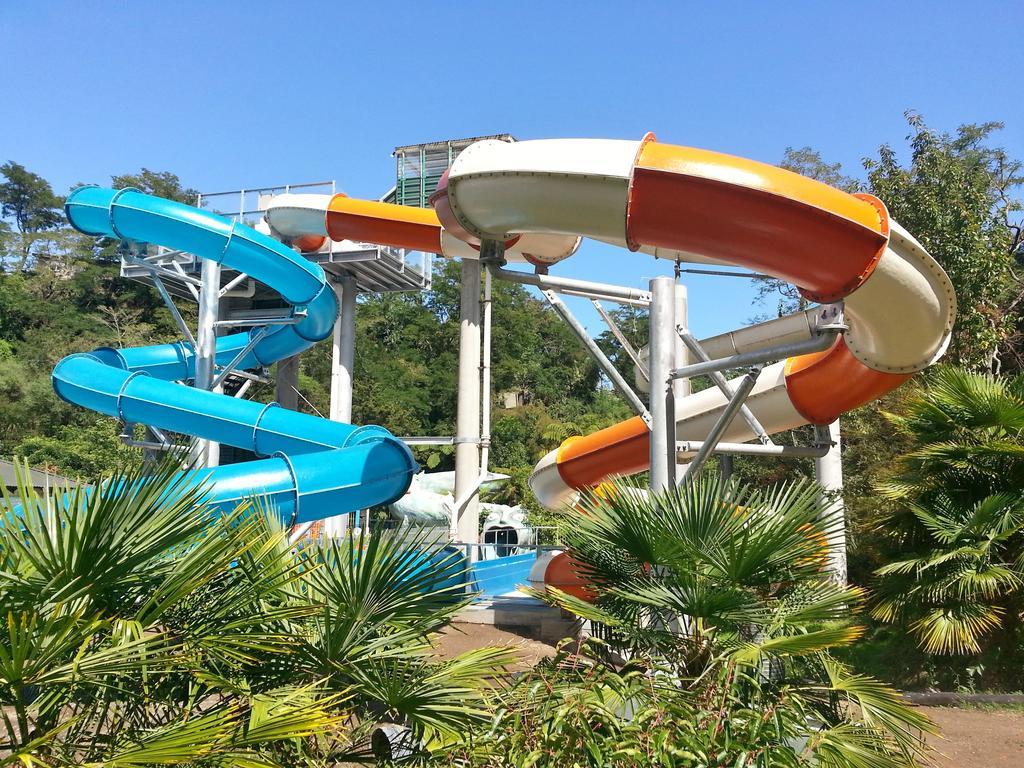 Taupo Debretts Spa Resort Luaran gambar The photo shows a water park featuring two large water slides. One slide is blue and curves gracefully, while the other is orange and white, twisting as it descends. They are supported by a metal structure and surrounded by lush greenery, including p
