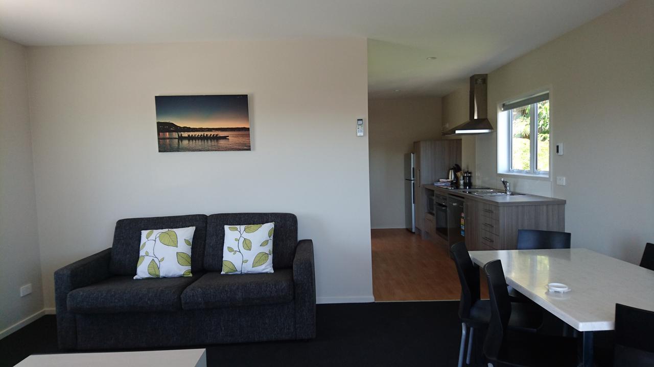 Taupo Debretts Spa Resort Luaran gambar The photo shows a modern living space that includes a living area and a kitchen. The living area features a dark sofa with two decorative pillows that have a leaf pattern. There is a framed picture on the wall, depicting a scenic view, possibly of a 