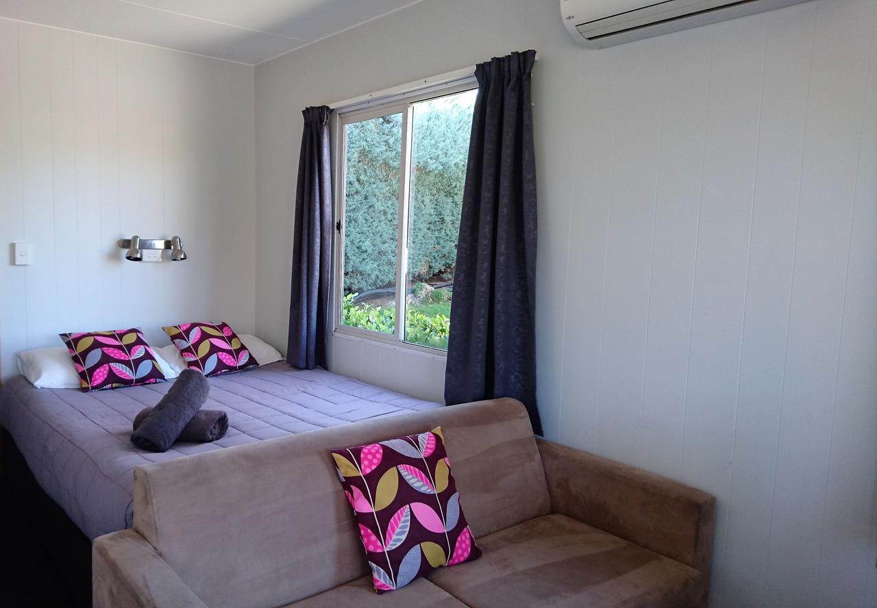Taupo Debretts Spa Resort Luaran gambar The photo shows a cozy room featuring a bed with colorful patterned cushions and a brown sofa. There are two large windows with dark curtains, allowing natural light to brighten the space. The walls are painted in a light color, and there are some pl