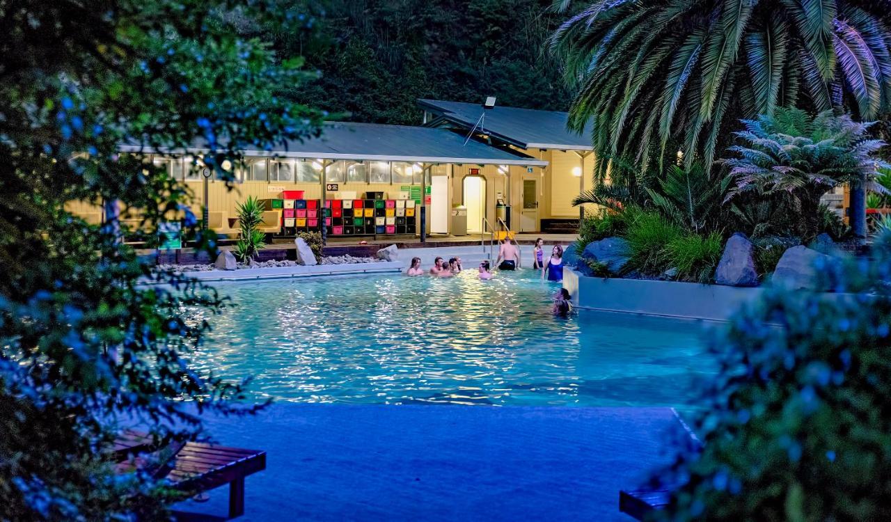 Taupo Debretts Spa Resort Luaran gambar The photo shows a scenic pool area illuminated by soft lighting during the evening. People can be seen enjoying the water, suggesting a relaxed atmosphere. In the background, there's a building with large windows, which appears to be part of a facili