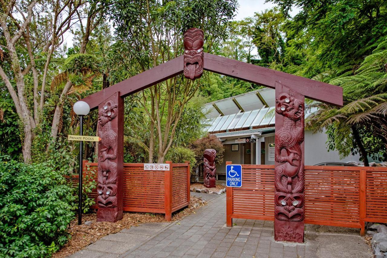 Taupo Debretts Spa Resort Luaran gambar The photo shows an entrance with a large archway that features intricate carvings. The arch is supported by two vertical posts, each adorned with detailed figures likely representing cultural symbols or characters. Surrounding the entrance are lush g