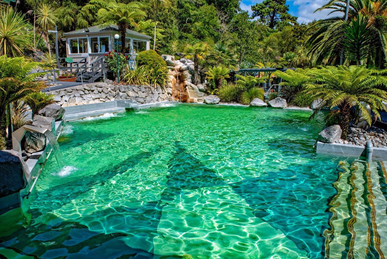 Taupo Debretts Spa Resort Luaran gambar The photo showcases a vibrant, natural-looking pool with crystal-clear, turquoise water. Surrounding the pool are lush green plants and palm trees, creating a tropical atmosphere. In the background, there is a white building, possibly a facility or a