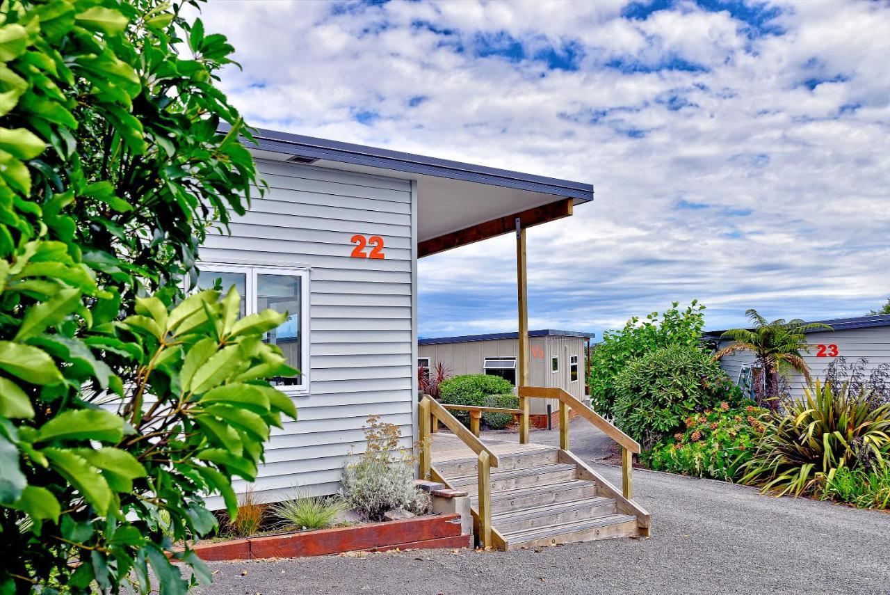Taupo Debretts Spa Resort Luaran gambar The photo shows a building, likely a cabin or cottage, with a wooden porch and stairs leading up to it. The structure has light-colored siding and the number "22" is prominently displayed on the side. Surrounding the building are various plants and t
