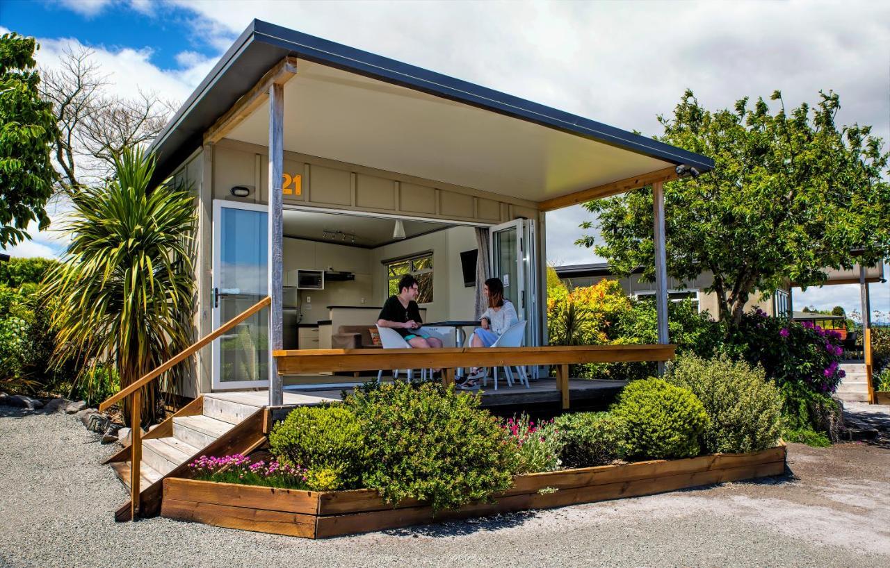 Taupo Debretts Spa Resort Luaran gambar The photo depicts a modern small house or cabin, featuring a covered porch with a wooden railing. Two people are seated at a table on the porch, engaging in conversation. The exterior of the house is designed with large windows, allowing ample natura